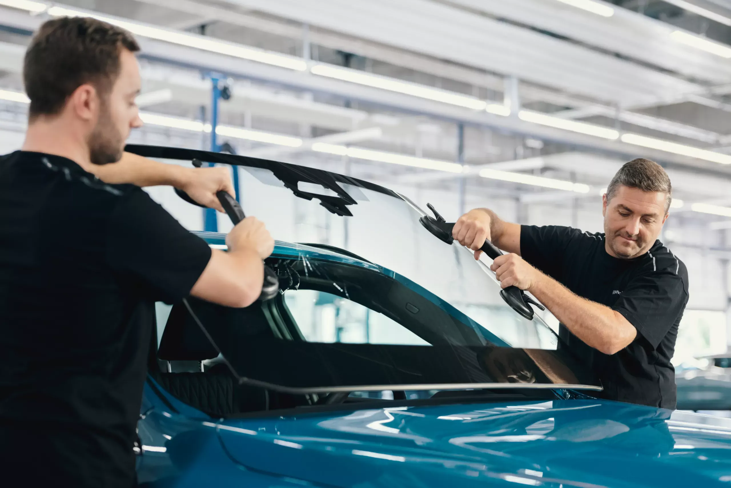 Deux mécaniciens BMW changeant le pare-brise d'une voiture BMW.
