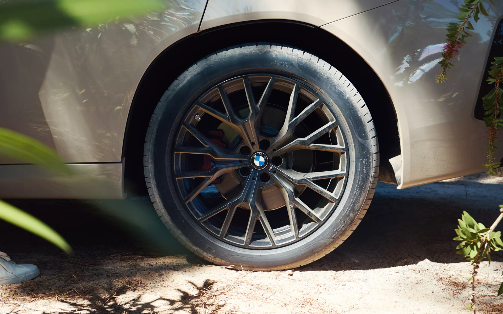 Gros plan sur une jante BMW sport en été, garée dans un chemin boisé.